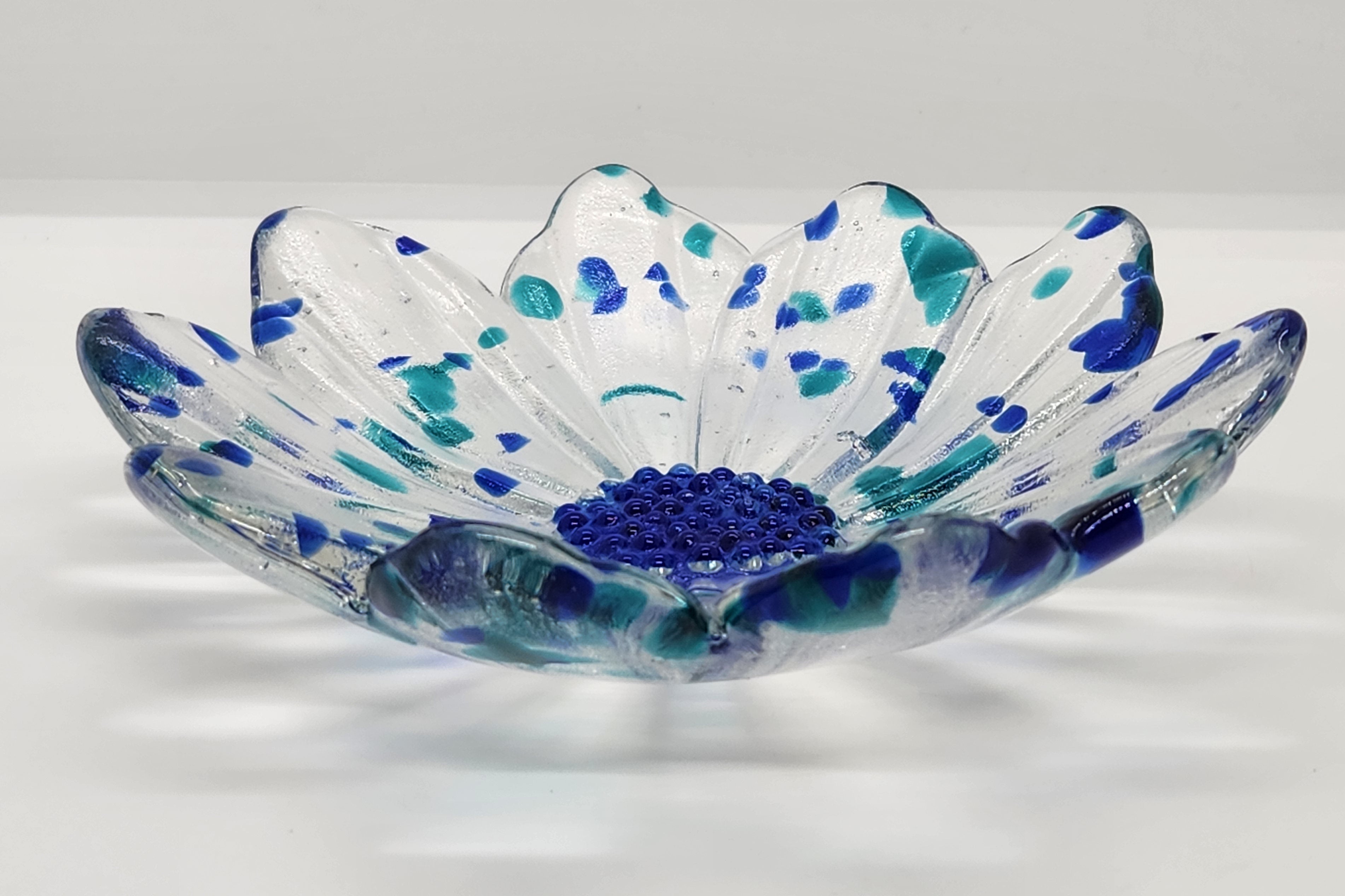 clear glass flower with blue center and blue flecks of glass on  a white background