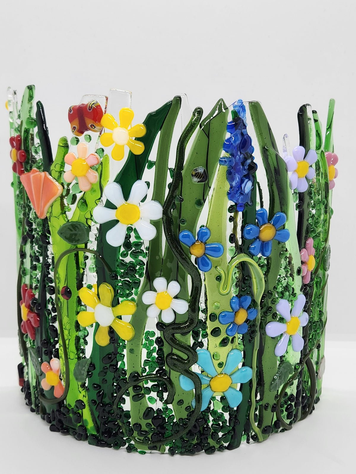 Curved fused glass Field of Flowers candle holder with colorful wildflowers, green grass, butterflies, bees, and ladybugs, designed to display beautifully with candlelight.