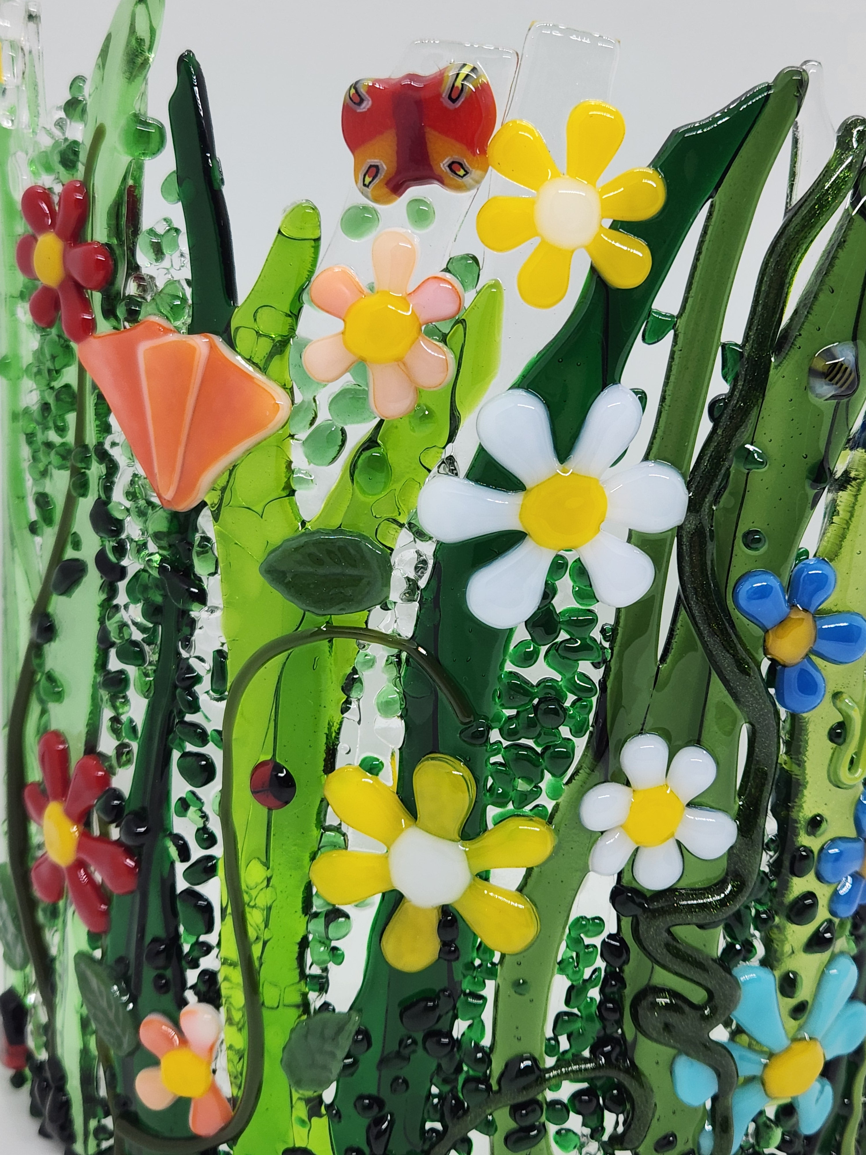 Curved fused glass Field of Flowers candle holder with colorful wildflowers, green grass, butterflies, bees, and ladybugs, designed to display beautifully with candlelight.