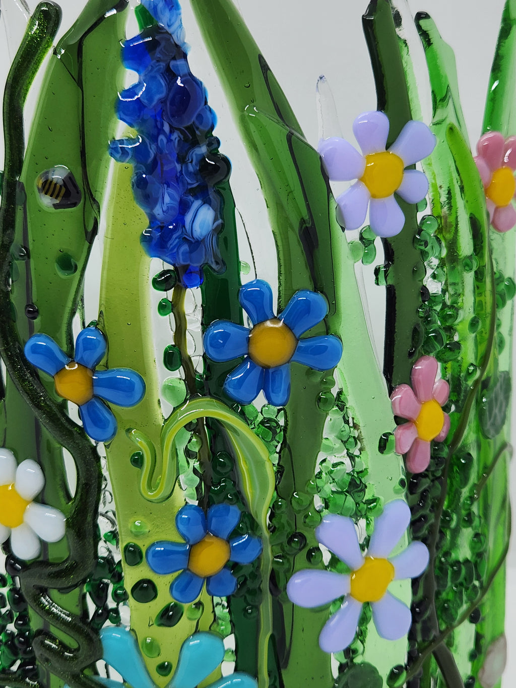 Curved fused glass Field of Flowers candle holder with colorful wildflowers, green grass, butterflies, bees, and ladybugs, designed to display beautifully with candlelight.