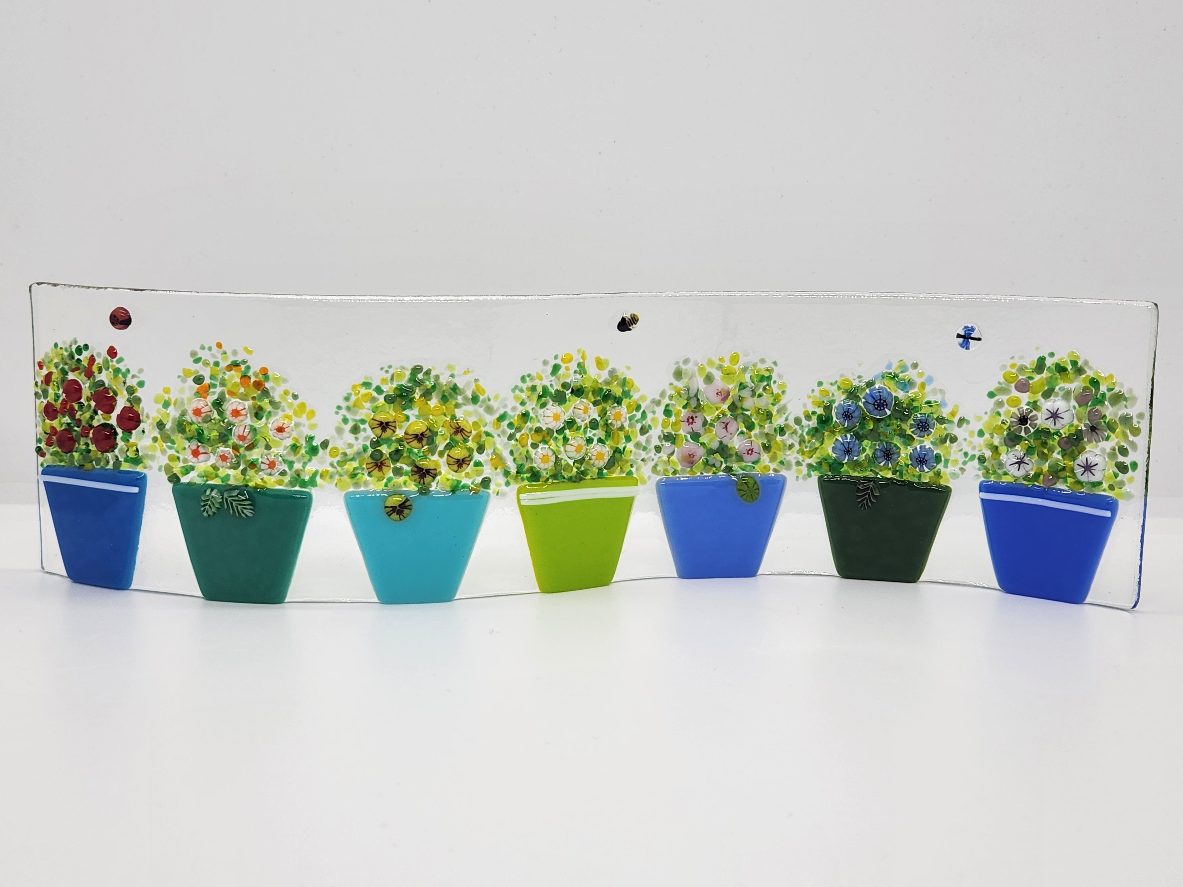 Fused glass Flower Pot Waves featuring blue and green flower pots with blooming greenery on a gently curved glass panel for home decor.