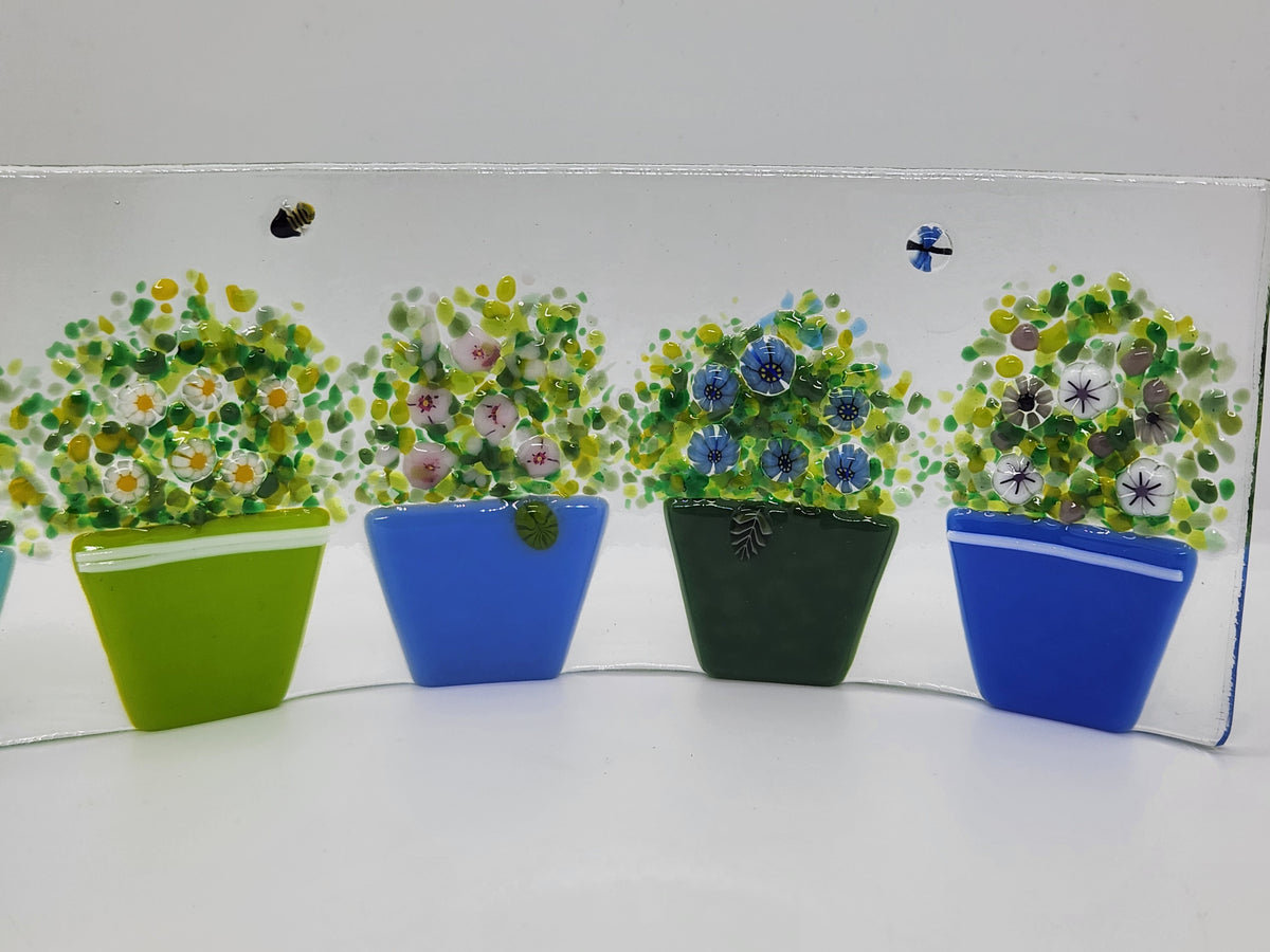 Fused glass Flower Pot Waves featuring blue and green flower pots with blooming greenery on a gently curved glass panel for home decor.