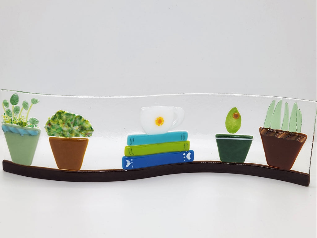Fused glass Book Shelf Wave featuring colorful books, potted plants, and garden-inspired details on a gently curved glass panel for home decor.