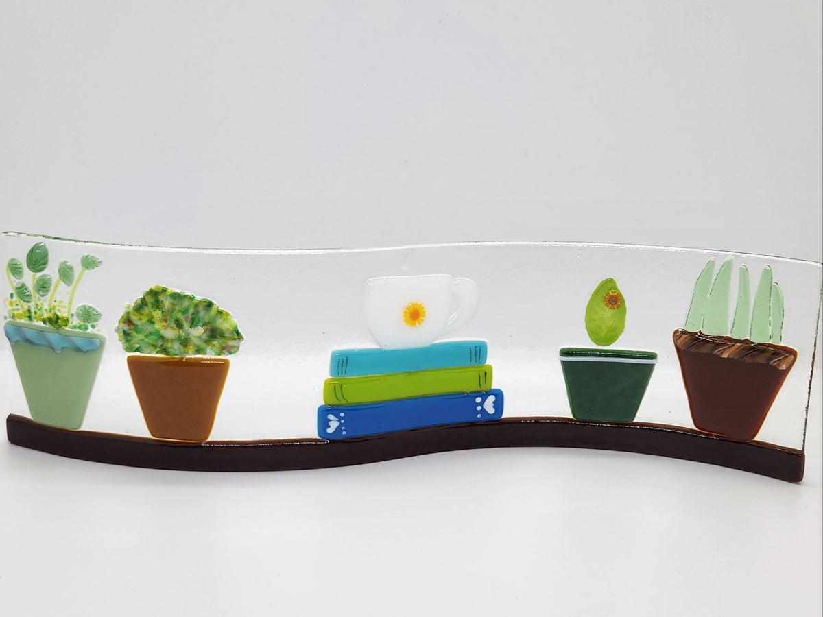 Fused glass Book Shelf Wave featuring colorful books, potted plants, and garden-inspired details on a gently curved glass panel for home decor.