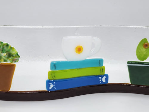 Fused glass Book Shelf Wave featuring colorful books, potted plants, and garden-inspired details on a gently curved glass panel for home decor.