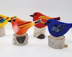 five colorful birds on birchwood stand in colors: light and dark blue, red, orange, and yellow.