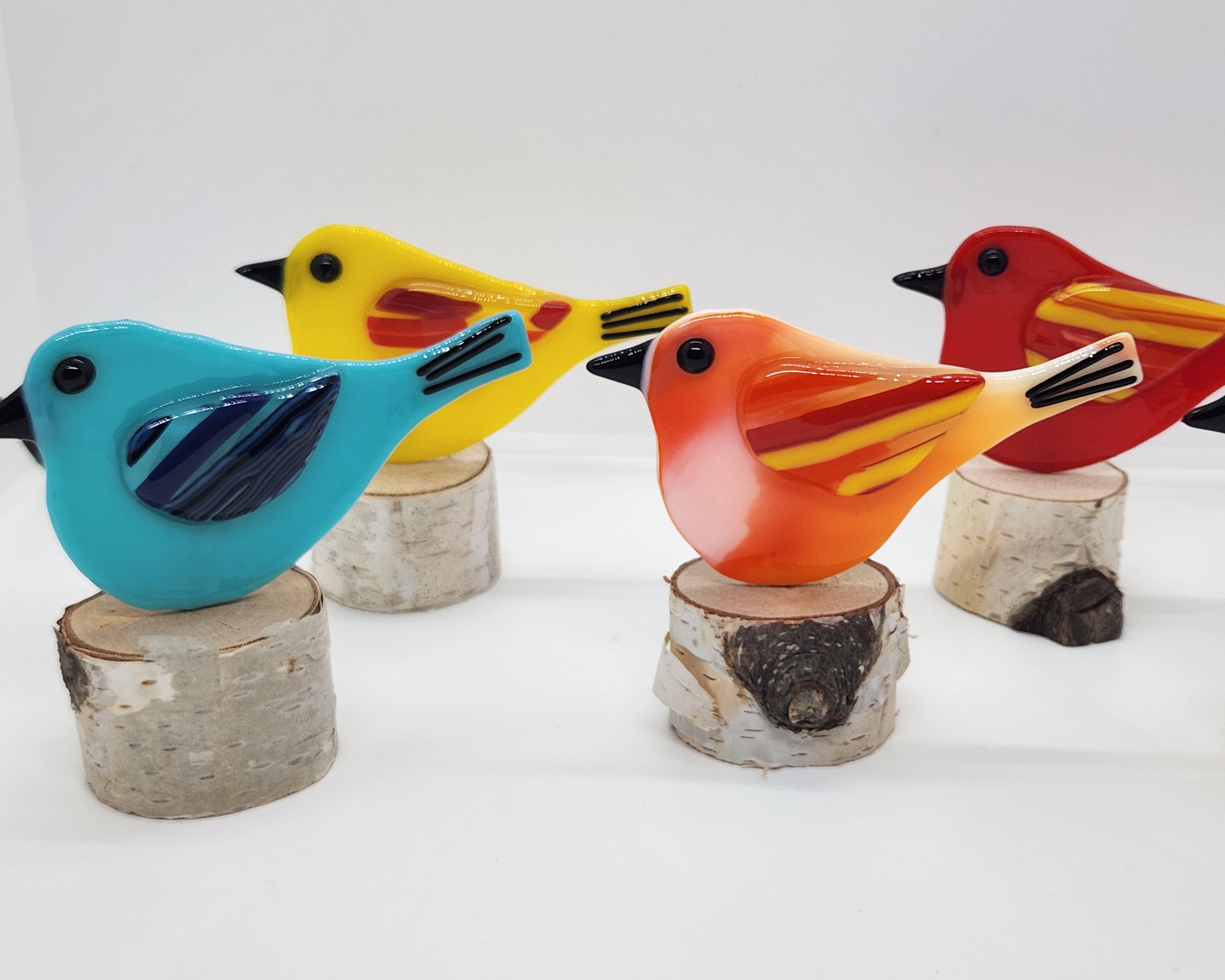 five colorful birds on birchwood stand in colors: light blue, red, orange, and yellow.