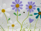Fused glass floral panel featuring lavender, turquoise, white, and blue daisies with whimsical garden details and a gently curved design for home decor.