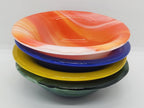 A stack of four hand-fused glass bowls in vibrant colors: orange and white marbled on top, followed by blue, yellow, and dark green.