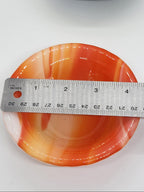 An orange and white marbled glass trinket dish shown with a metal ruler to indicate its size.