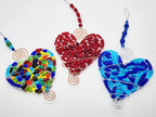 Three heart suncatchers in colors: rainbow, red, and blue. They have copper and silver wire wraps which are beaded
